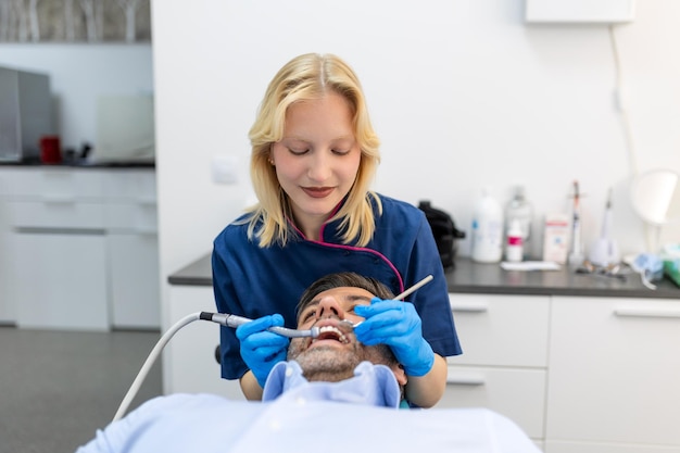Dentista en uniforme azul haciendo procedimiento de dientes a paciente masculino durante el procedimiento de tratamiento en clínica dental contemporánea