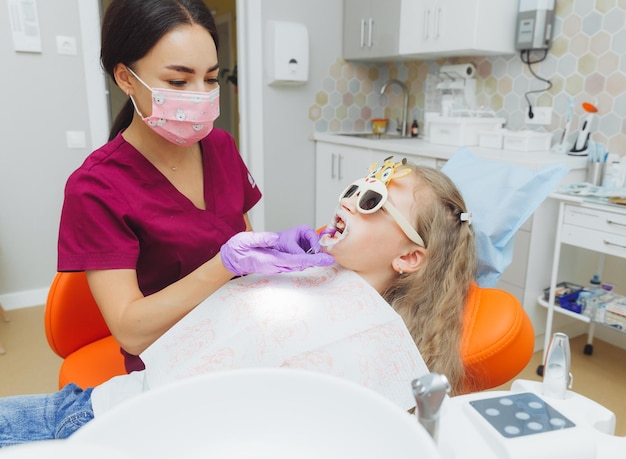 Dentista usando un dique de goma mientras examina a una niña paciente con un retractor de mejillas en la boca