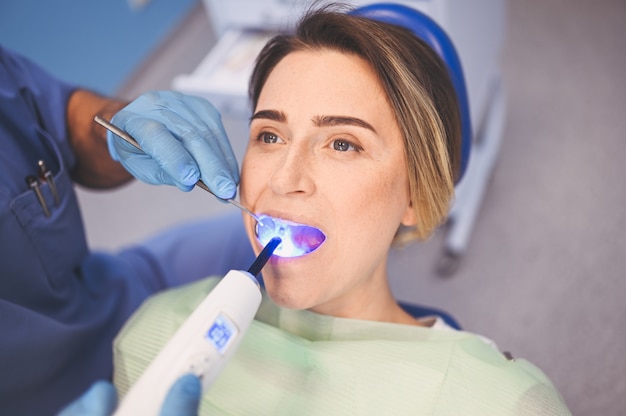 Dentista usando luz de cura dental para preencher os dentes de um paciente no consultório odontológico