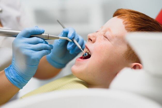 Dentista usando máscara. Dentista infantil ruivo usando máscara examinando menino bonito