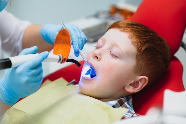 Dentista usando máscara. Dentista infantil ruivo usando máscara examinando menino bonito