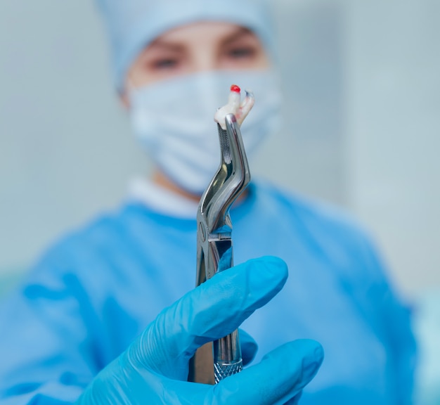 Dentista usando um alicate cirúrgico para remover um dente em decomposição. clínica odontológica moderna