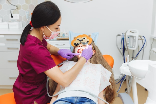 Dentista usando uma barragem de borracha enquanto examina uma menina paciente com um retrator de bochecha na boca