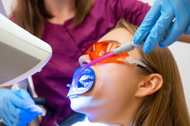 Un dentista utilizando un eyector de saliva durante el tratamiento de blanqueo de dientes para un paciente joven