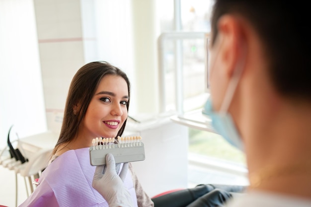 Foto dentista verificando e selecionando a cor dos dentes da jovem