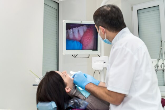 Dentista verificando os dentes do paciente com a câmera, olhando na tela