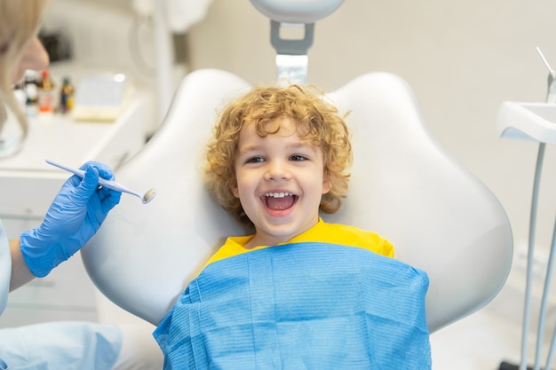 Dentista de visita del muchacho joven lindo, teniendo sus dientes revisados por dentista en el consultorio dental.