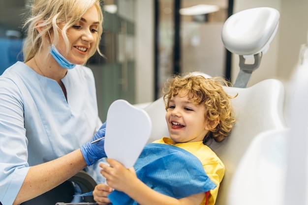 Dentista de visita del muchacho joven lindo, teniendo sus dientes revisados por dentista en el consultorio dental.