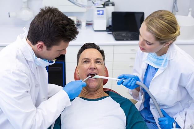 Foto dentistas examinando a un paciente masculino con herramientas