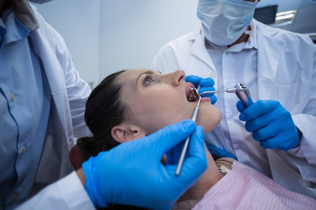 Dentistas examinando uma paciente do sexo feminino com ferramentas