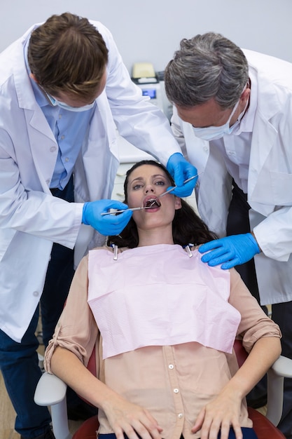 Dentistas examinando uma paciente do sexo feminino com ferramentas