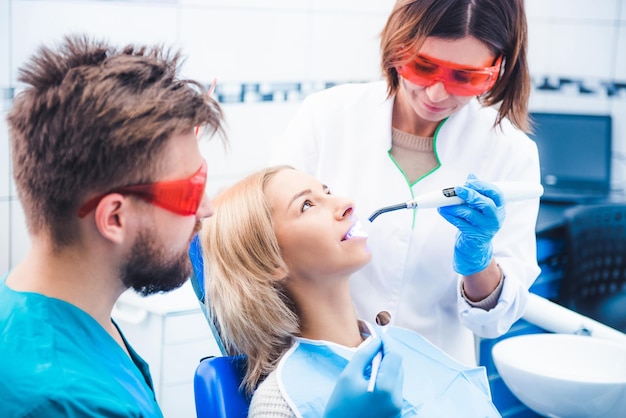 Foto dentistas en gafas rojas que encienden el sello dental con lámpara ultravioleta