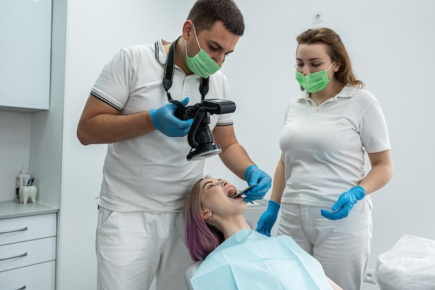 Los dentistas masculinos y femeninos toman fotos profesionales de la cavidad oral de una niña, fotos antes y después del progreso del tratamiento.