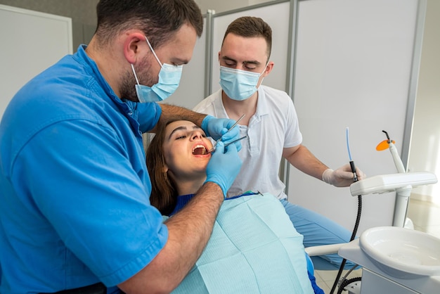 Dentistas con taladro de espejo y rociador de pistola de agua de aire dental que tratan los dientes de pacientes adultos en la clínica dental