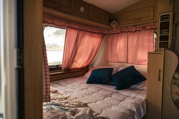 Dentro de ninguém camper van com cama, travesseiro, cortina na janela do acampamento. Atividades de lazer nas férias