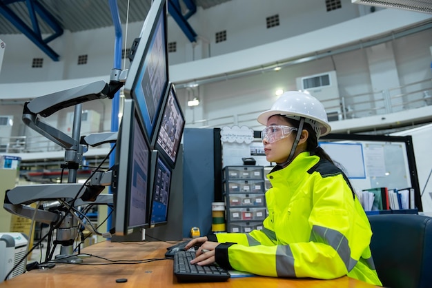 Dentro de la gran fábrica de la industria, una ingeniera informática trabaja en una computadora personal. Programa de codificación para la máquina de control. La gente de Tailandia trabaja en cuatro monitores.