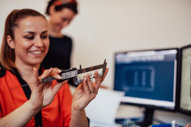 Foto dentro de la industria pesada, un ingeniero industrial de fábrica mide con una pinza y en una computadora personal diseña un modelo 3d