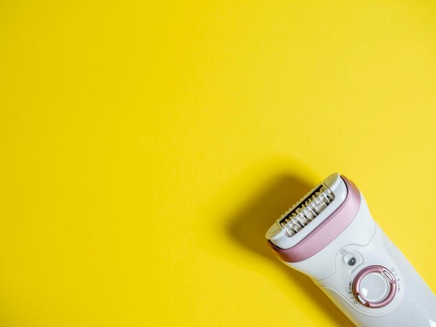 Depiladora eléctrica femenina sobre un fondo amarillo Copie el espacio un concepto para dispositivos de belleza y cuidado personal