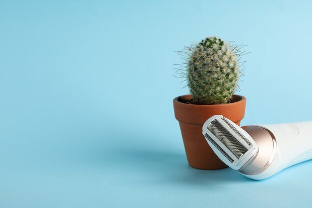 Foto depiladora y jarrón con cactus sobre fondo azul.