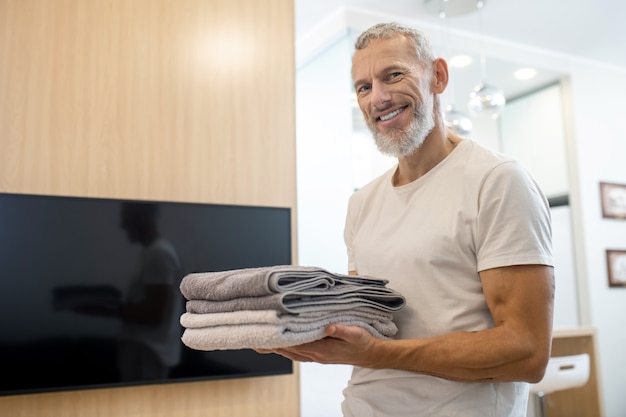 Depois da lavanderia. Um homem com uma camiseta branca segurando toalhas e sorrindo gentilmente