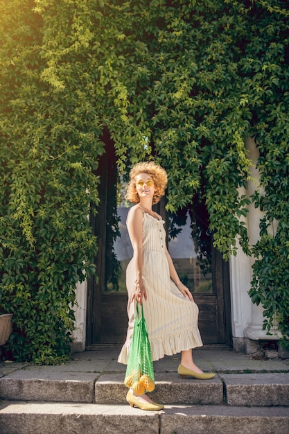 Depois das compras. Foto de uma jovem com um vestido branco e uma bolsa de rede com frutas nas mãos