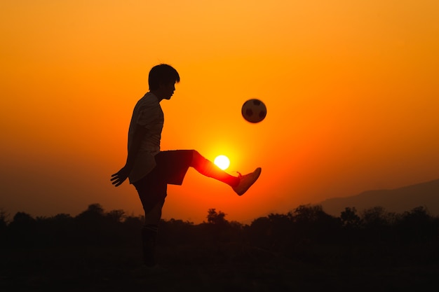 Foto deporte de acción silueta al aire libre de joven divirtiéndose jugando fútbol soccer para hacer ejercicio bajo la puesta de sol.