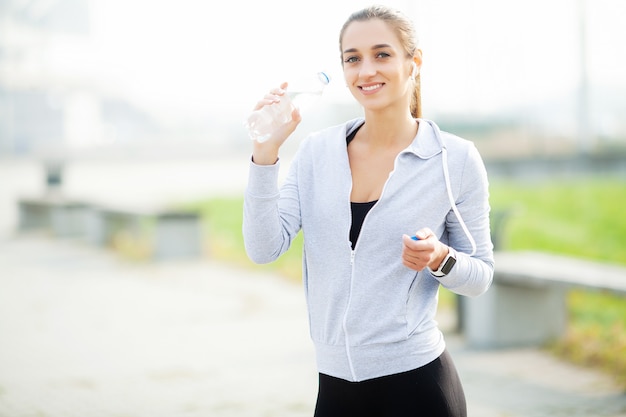 Deporte al aire libre. Deportiva mujer en auriculares agua potable