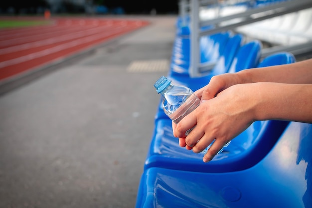 Deporte y bienestar. Descanse después del entrenamiento, beba agua para el cuidado de la salud y los deportes al aire libre en las mañanas en verano. Mujer milenaria sosteniendo una botella en el estadio exterior, de cerca, espacio de copia