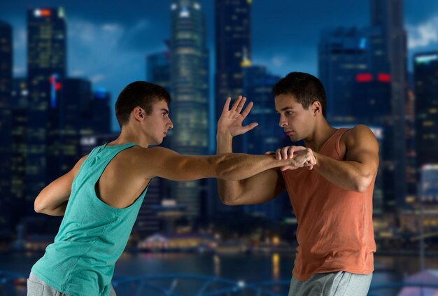 deporte, competencia, fuerza y concepto de la gente - hombres jóvenes que luchan mano a mano sobre el fondo de la ciudad nocturna