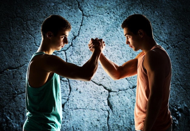 Foto deporte, competición, fuerza y concepto de la gente - dos jóvenes luchan con los brazos sobre el fondo de la pared de hormigón
