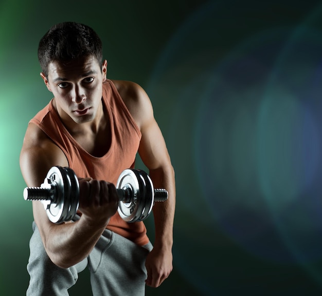 deporte, culturismo, entrenamiento y concepto de personas - joven con bíceps flexionando mancuernas sobre fondo oscuro