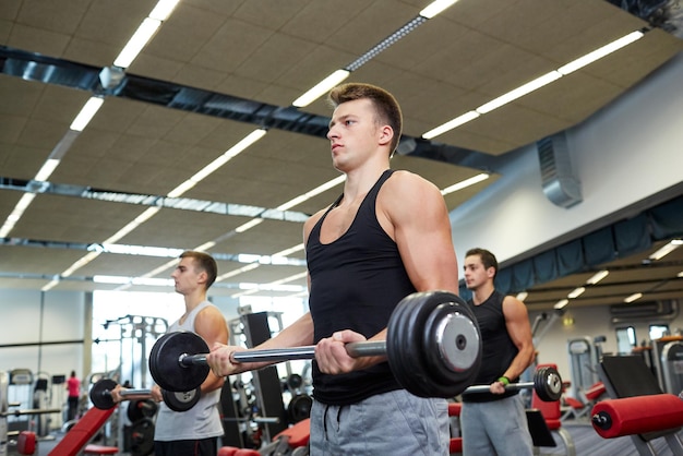 deporte, culturismo, estilo de vida y concepto de personas - grupo de hombres con músculos flexionados con barra en el gimnasio