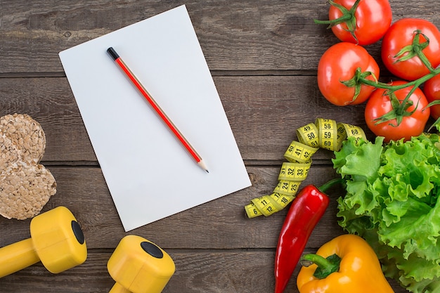 Foto deporte y dieta verduras pesas y ensalada de tomates pimientos centímetro sobre fondo rústico