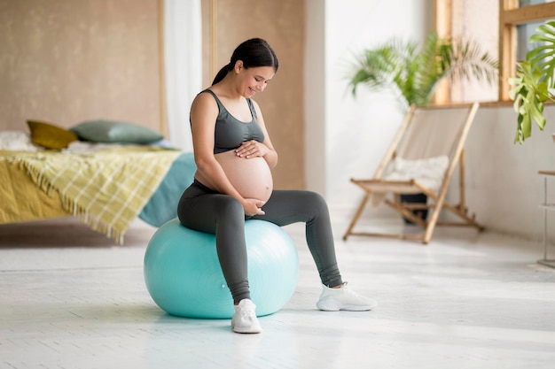 Deporte durante el embarazo Hermosa mujer embarazada sentada en Fitball y abrazando el vientre