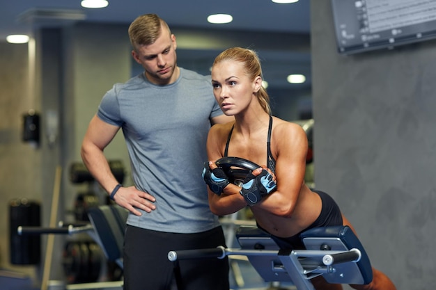 Deporte, entrenamiento, condición física, estilo de vida y concepto de la gente - mujer joven con un entrenador personal que dobla la espalda y los músculos abdominales en un banco en el gimnasio