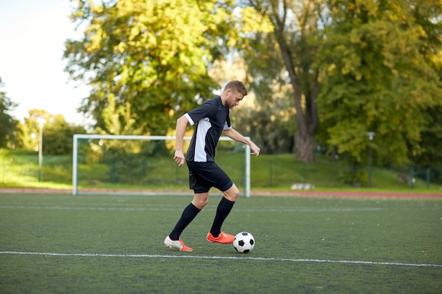 deporte, entrenamiento de fútbol y gente - futbolista jugando con pelota en el campo