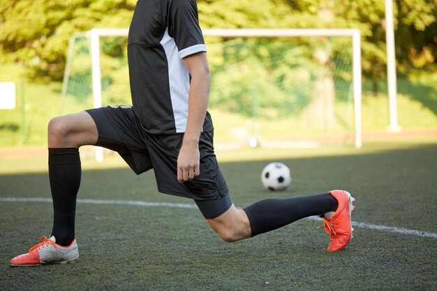 Foto deporte, entrenamiento de fútbol y gente - jugador de fútbol estirando la pierna en el campo