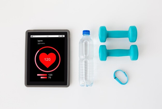 deporte, estilo de vida saludable, concepto de fitness y tecnología: cierre de la frecuencia cardíaca de la computadora de la tableta en la pantalla, mancuernas con rastreador de fitness y botella de agua sobre fondo blanco