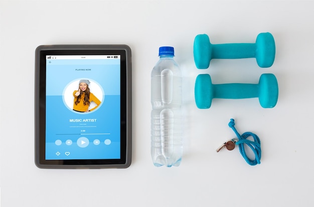 deporte, estilo de vida saludable, concepto de fitness y tecnología - tablet pc con pesas, silbato y botella de agua sobre fondo blanco