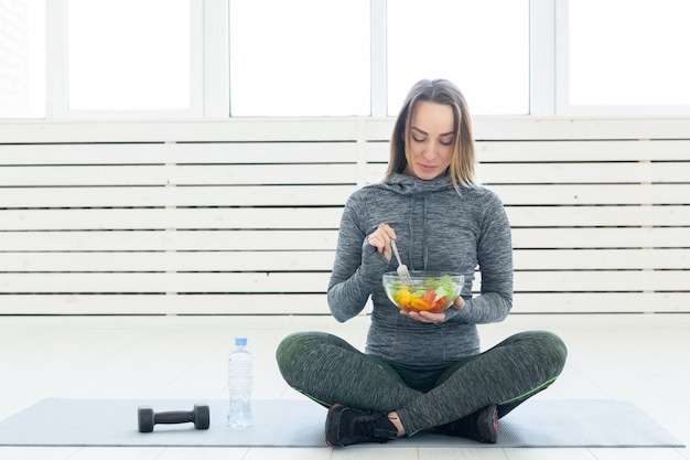 Deporte estilo de vida saludable y concepto de gente joven con ensalada y una pesa sentada en el