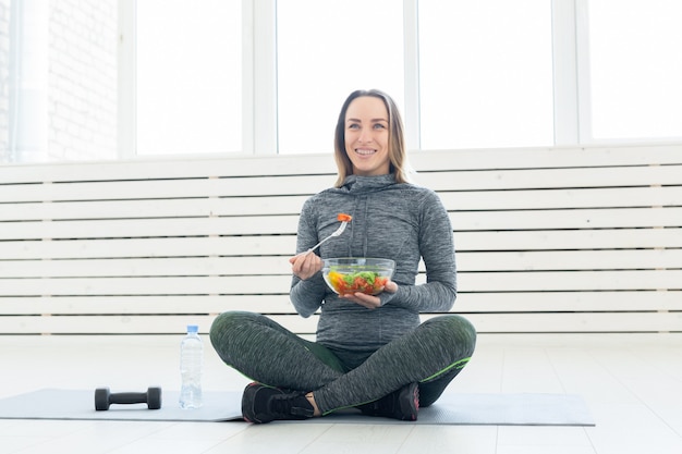 Deporte estilo de vida saludable y concepto de gente joven con ensalada y una pesa sentada en el