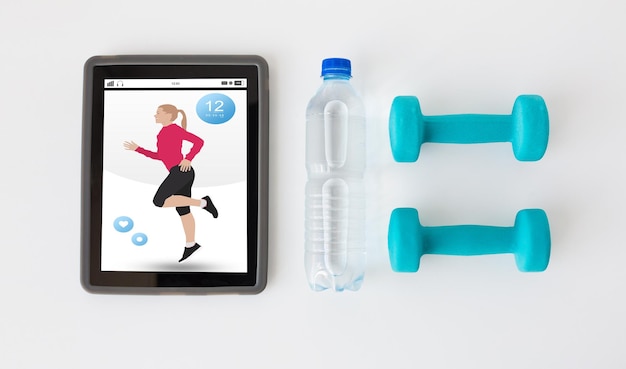 deporte, estilo de vida saludable, fitness, tecnología y concepto de objetos: cierre de una tableta con pesas y una botella de agua sobre fondo blanco