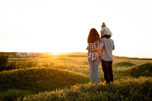 Deporte familia al atardecer Padre, madre e hija en un paseo en verano divertirse y jugar Papá tiene un hijo sobre sus hombros Concepto de relaciones familiares felices Lugar para el texto