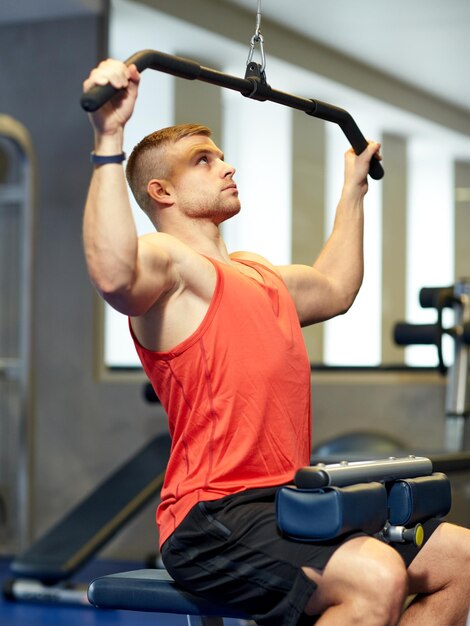 deporte, fitness, culturismo, estilo de vida y concepto de personas - hombre haciendo ejercicio y flexionando los músculos en la máquina de cable en el gimnasio