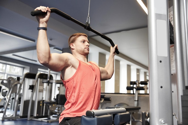 deporte, fitness, culturismo, estilo de vida y concepto de personas - hombre haciendo ejercicio y flexionando los músculos en la máquina de cable en el gimnasio