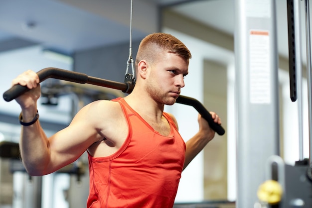 deporte, fitness, culturismo, estilo de vida y concepto de personas - hombre haciendo ejercicio y flexionando los músculos en la máquina de cable en el gimnasio