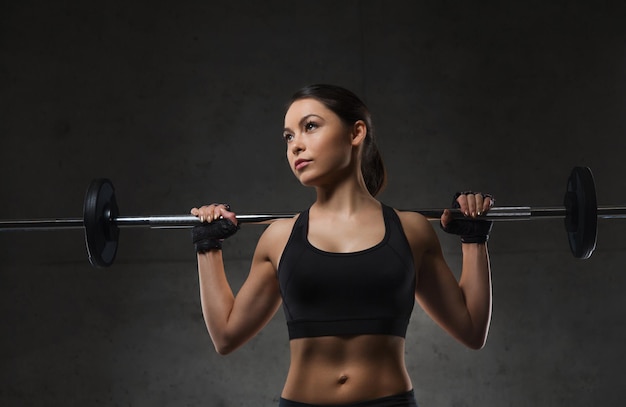 deporte, fitness, culturismo, levantamiento de pesas y concepto de personas - mujer joven con músculos flexionados con barra en el gimnasio