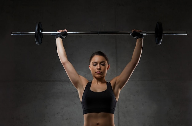 deporte, fitness, culturismo, levantamiento de pesas y concepto de personas - mujer joven con músculos flexionados con barra en el gimnasio