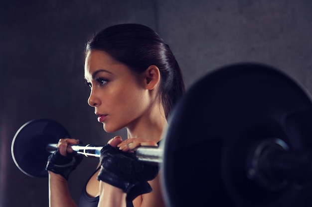 deporte, fitness, culturismo, levantamiento de pesas y concepto de personas - mujer joven con músculos flexionados con barra en el gimnasio