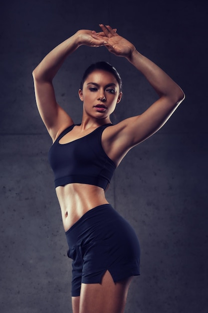 deporte, fitness, culturismo, levantamiento de pesas y concepto de personas - mujer joven posando y mostrando músculos en el gimnasio